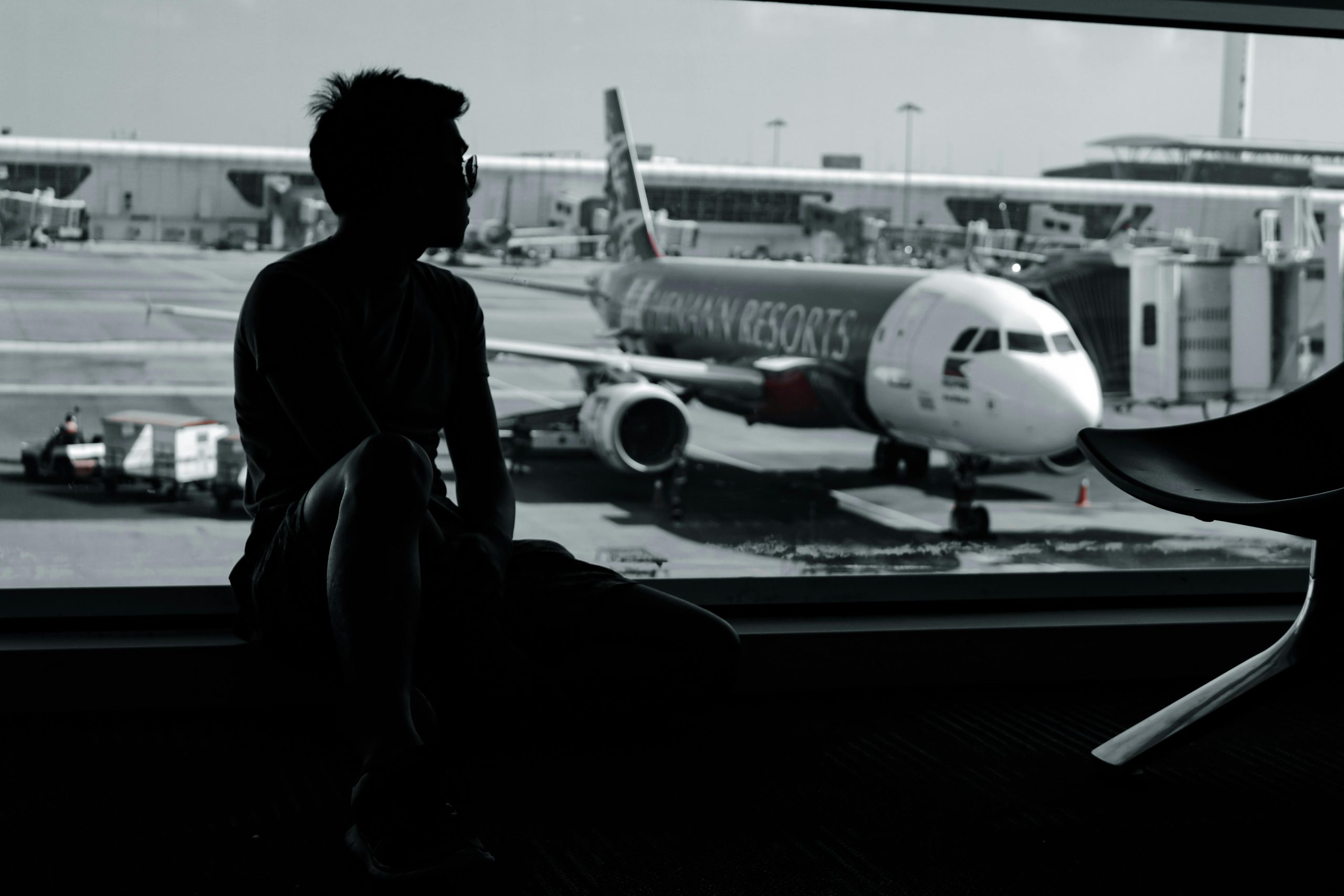 Silhouetted traveler at an airport gate lounge watching an aircraft on the apron