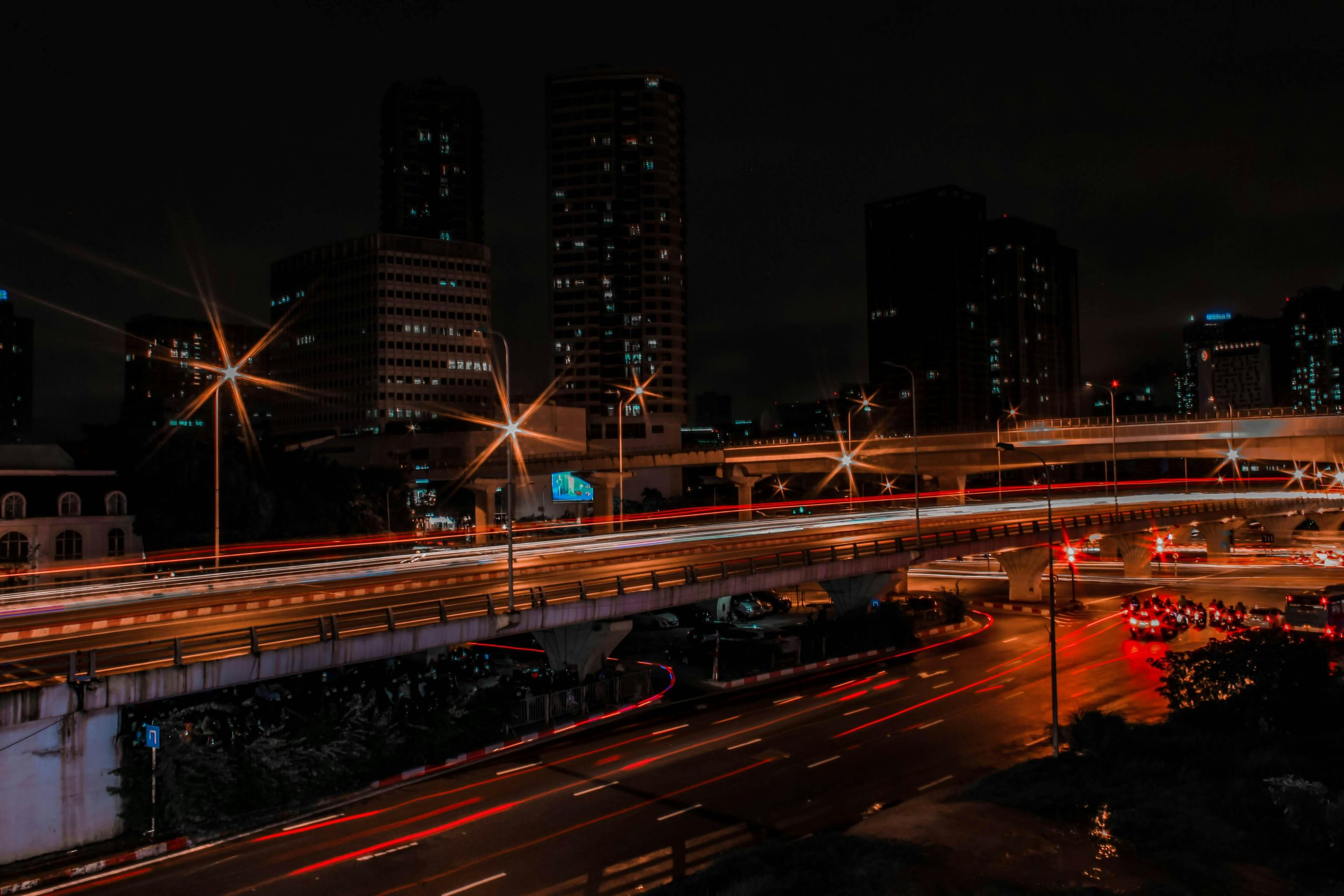 Night highway cutting through an Asian city skyline with car light trails and illuminated high-rises