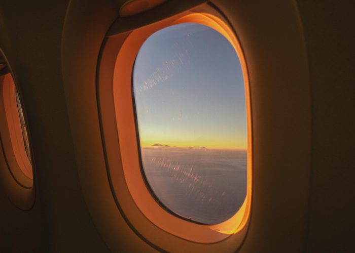 View through an airplane window at sunrise, clouds below and sky turning blue above