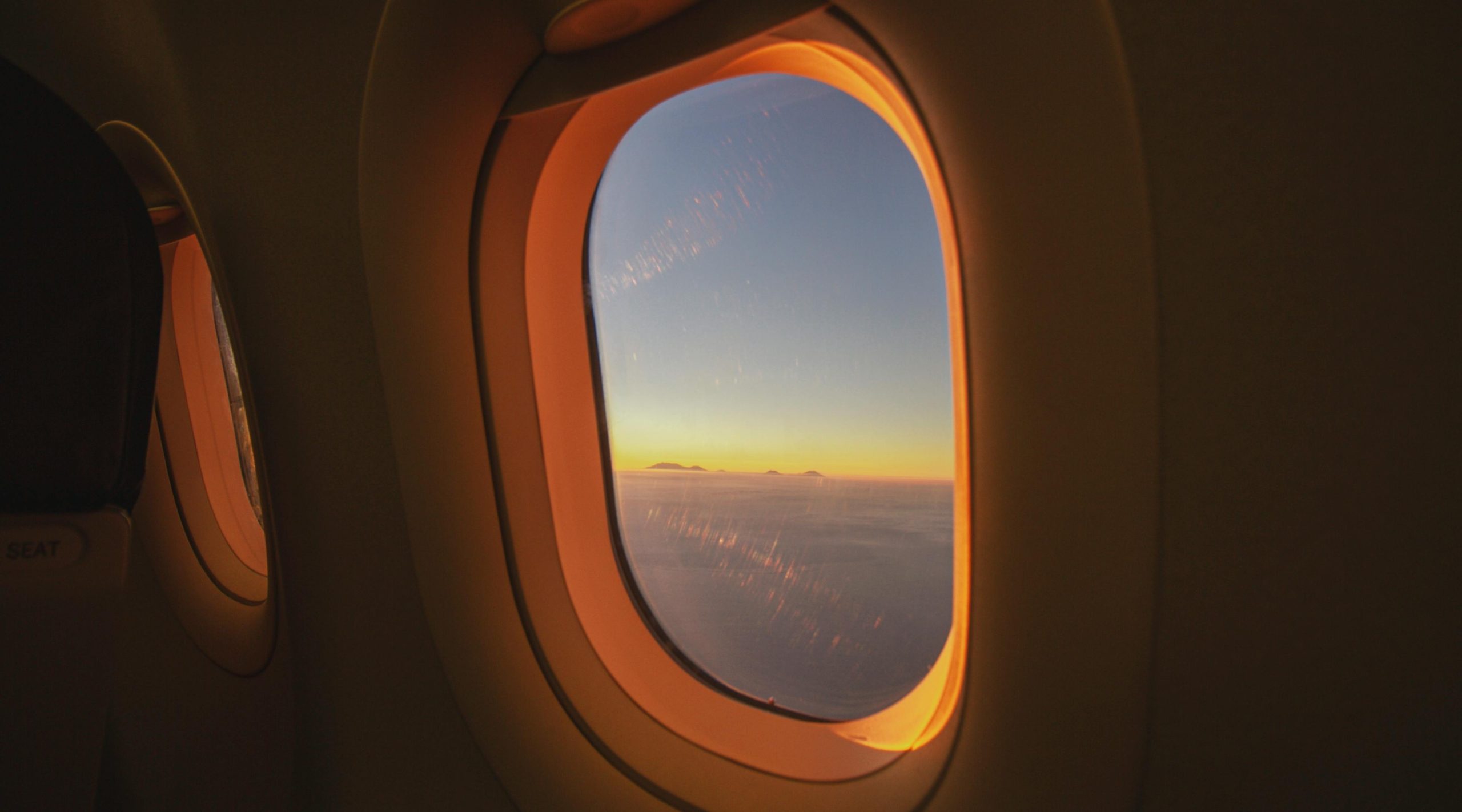 View through an airplane window at sunrise, clouds below and sky turning blue above