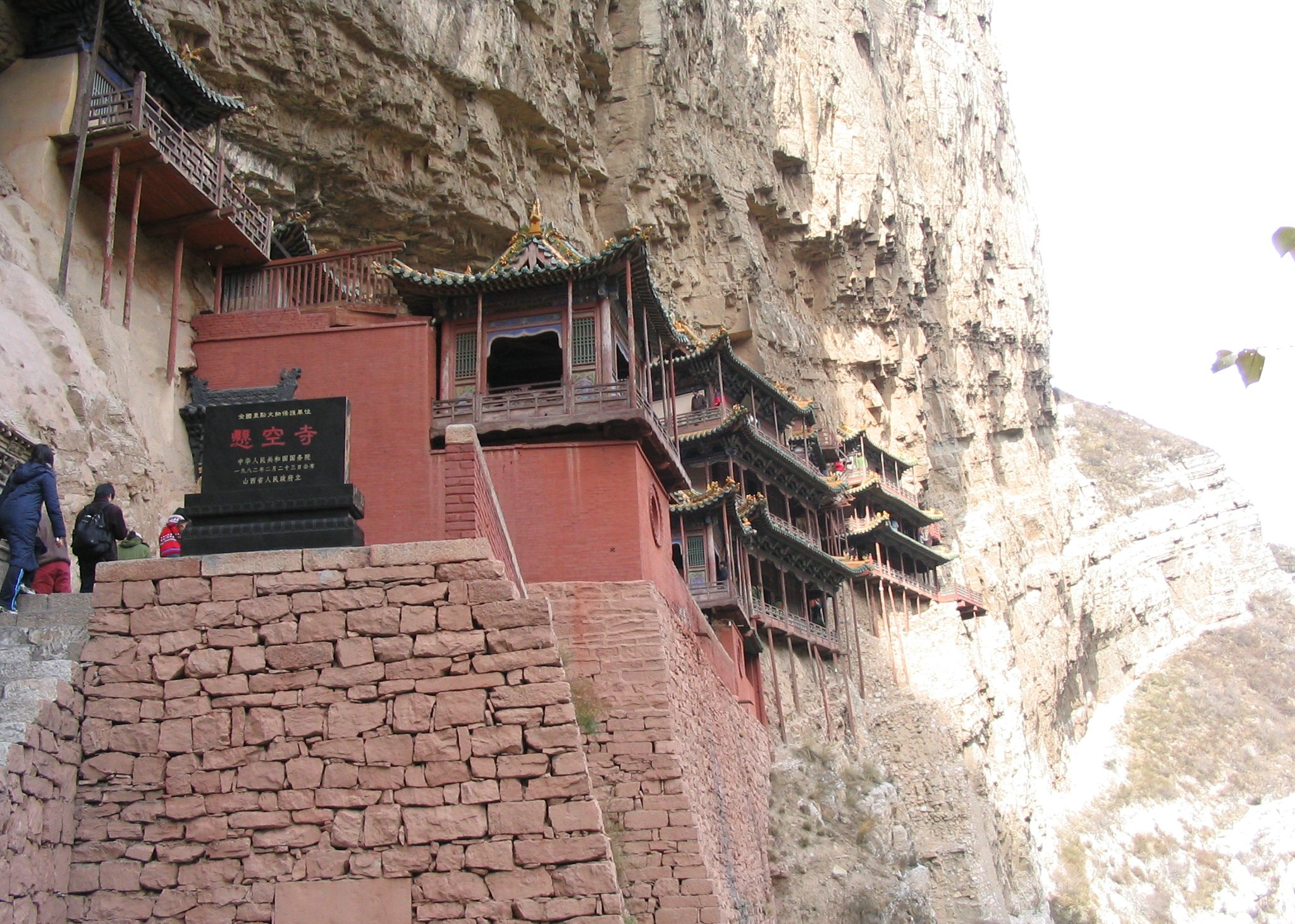 The Hanging Temple seen from the entrance walkway, with visitors approaching the multi-storey structure built into the cliff