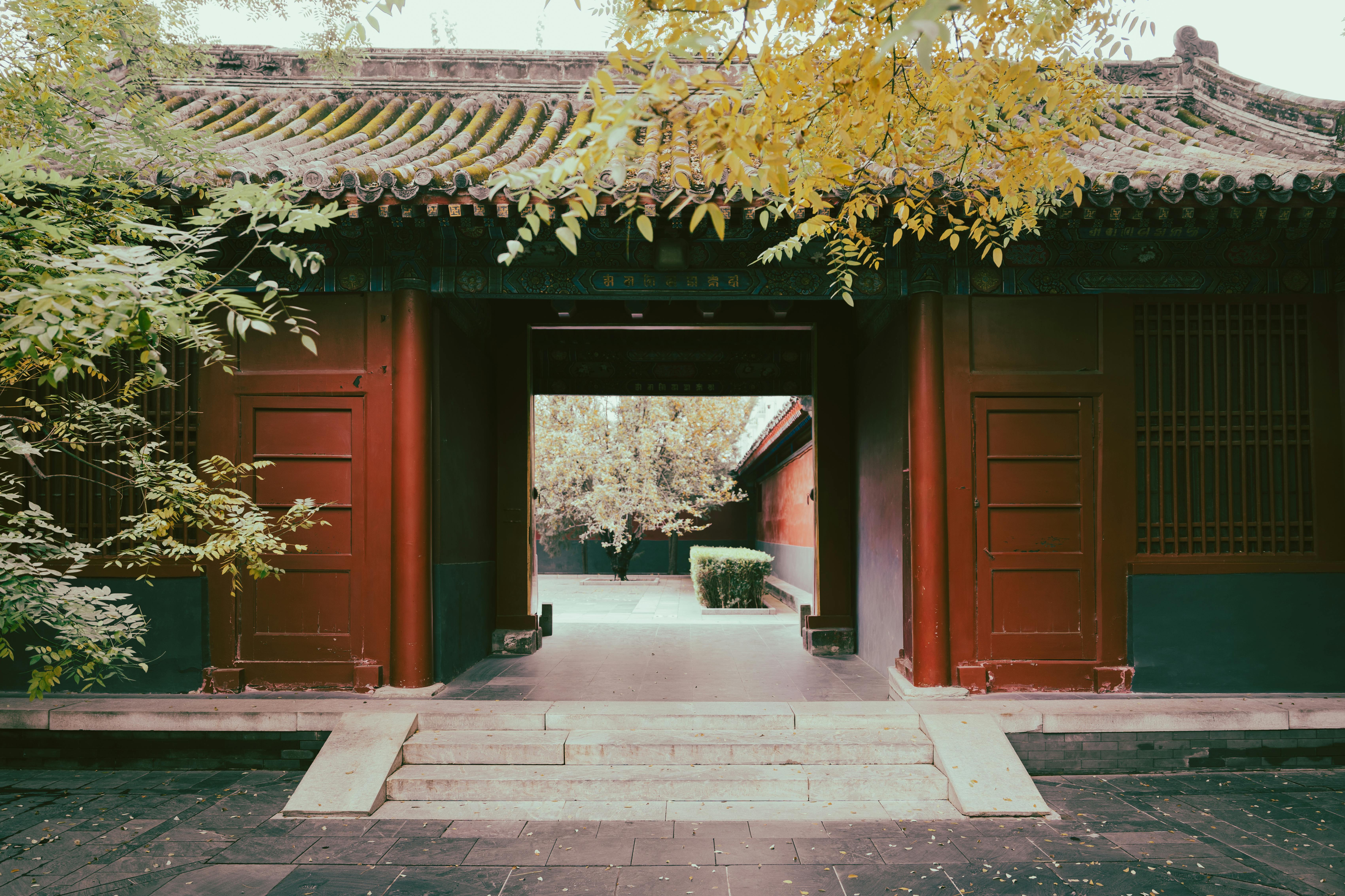 Traditional Chinese courtyard gate with red pillars and autumn foliage