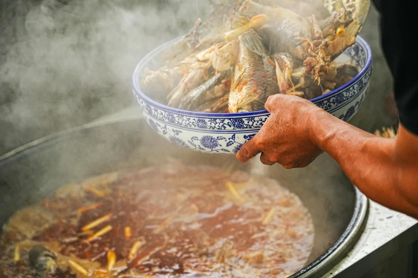 Seafood being poured into a steaming Chongqing hotpot with red chili oil